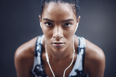 汗水摄影照片_一位活跃的年轻混血女性的肖像，脸上满是汗水，戴着耳机，在户外跑步或慢跑后休息。