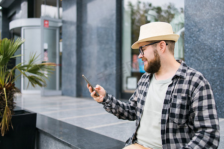 手机夏季夏季摄影照片_微笑的男性游客在夏季城市度假期间使用智能手机 — 技术和社交媒体应用程序概念