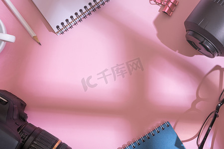 粉红色背景的顶视图笔记本电脑、单反相机、镜头和眼镜。