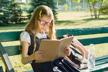 背书包的小学生摄影照片_背景学校院子里背着书包在长椅上看书的女小学生画像