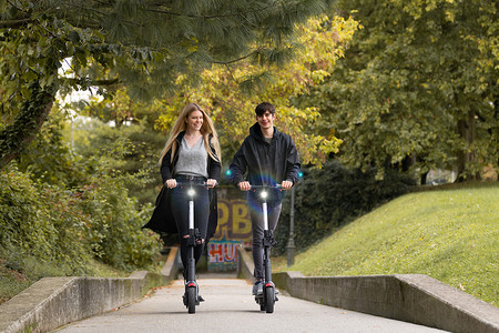 时髦时髦的青少年在城市公园里骑公共租赁电动滑板车。