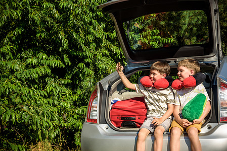 可爱小孩坐摄影照片_两个可爱的小孩男孩在离开去暑假前坐在汽车后备箱里。