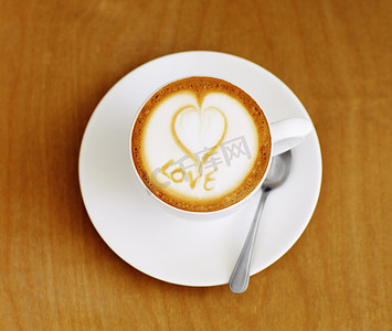 咖啡爱好者摄影照片_用充满爱意的双手制作……咖啡桌上精心准备的一杯卡布奇诺咖啡的高角度拍摄。