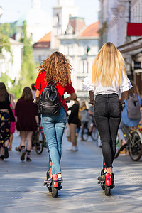 在城市环境中乘坐公共租赁电动滑板车的时尚时尚少女的后视图。