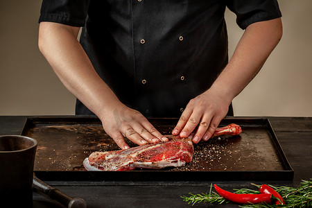 男厨师在木桌上的石盘上用盐和胡椒摩擦生羊腿。