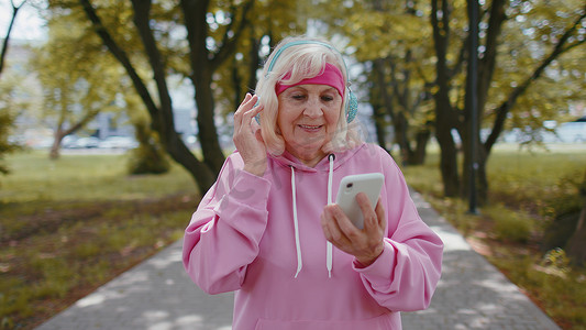 晨间公园戴耳机听智能手机音乐的运动高级运动跑步女性