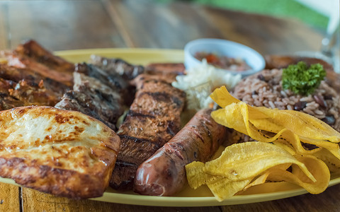烤牛肉配米饭、炸奶酪和番茄沙拉、木桌上供应的尼加拉瓜食物、木桌上摆着各种烤肉的盘子