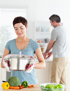 可爱的妻子拿着锅，而她的丈夫正在洗碗