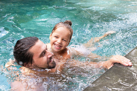幸福的家庭，活跃的父亲带着小孩，可爱的幼儿女儿，在游泳池里玩得很开心。