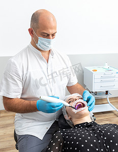 紫外线灯摄影照片_牙医在患者牙齿上使用牙科固化紫外线灯