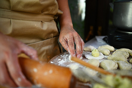 有选择地关注一位穿着米色厨师围裙的家庭主妇，在乡村厨房里擀面团、包饺子