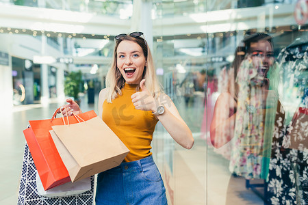 采集客户端摄影照片_快乐的年轻购物狂女人拿着纸袋购物，面带微笑