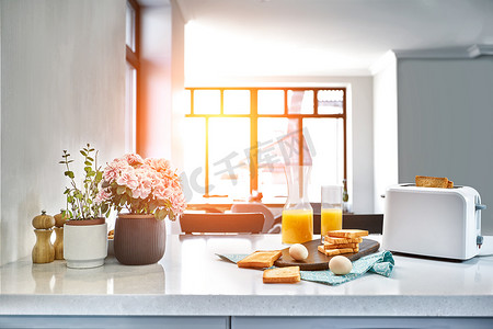面包鸡蛋橙汁摄影照片_烤面包机配有新鲜面包、鸡蛋和一杯橙汁，放在浅色的厨房桌子上。