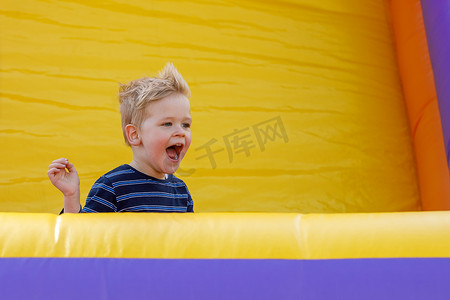 充气城堡摄影照片_小男孩在充气城堡游乐场玩得很开心。
