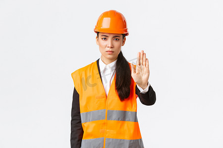 表情严肃、失望的亚洲女建筑师、工作区的施工经理戴着安全帽，表现出停止手势、禁止行动、禁止侵入、白色背景