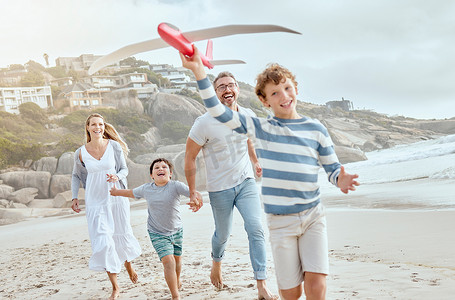 快乐的白人父母和孩子们一起玩玩具飞机，同时在海滩上度过一个轻松愉快的家庭暑假，享受美好时光。