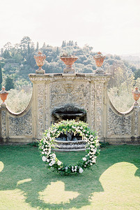 婚礼墙摄影照片_婚礼拱门矗立在一堵石墙上的喷泉前，里面有粘土双耳瓶