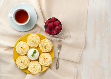 减肥奶酪煎饼，玫瑰形状，黄盘上有茶，覆盆子在纺织亚麻餐巾上