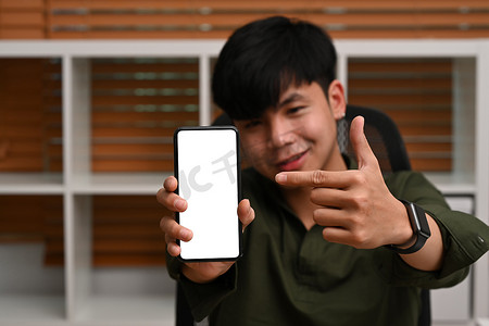 英俊的亚洲男子拿着和显示智能手机与空白屏幕做广告。