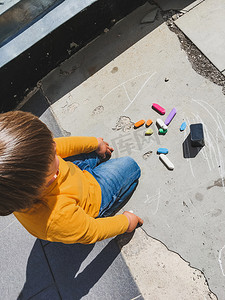 阳光明媚的日子里，穿着牛仔裤的幼儿用蜡笔在沥青上画画。