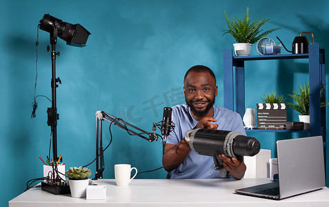 视频博客评论员在视频博客工作室中展示坐在办公桌前、配有笔记本电脑的新型视频灯