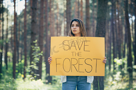 志愿者日摄影照片_森林里年轻漂亮的女志愿者活动家，张贴着拯救森林的海报