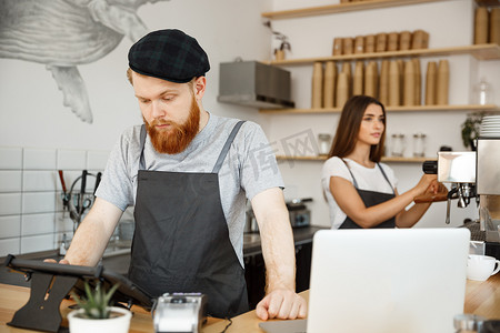咖啡经营理念-年轻英俊的留着胡子的调酒师、咖啡师或经理在现代咖啡店的数字平板电脑菜单中发布客人的订单。
