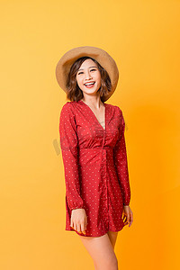 橙色背景中身穿红色连衣裙、头戴草帽、快乐、精力充沛的亚洲女性的摄影棚照片