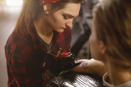 创意时尚画摄影照片_戴着防护手套的纹身艺术家开始在客户手臂上画纹身