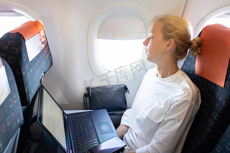 在旅行期间摄影照片_疲惫的女商人在出差期间在飞机上打盹。