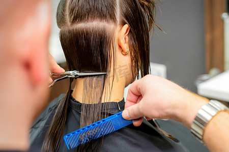 美容院里，男理发师用剪刀和梳子给女顾客剪头发。