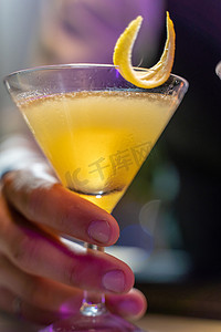夜总会吧台上，酒保的手端着一杯带有柠檬皮的漂亮黄色鸡尾酒的特写。