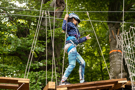 小女孩学龄前儿童穿着完整的攀岩安全带，使用登山扣和其他安全设备在绳索公园玩得很开心。