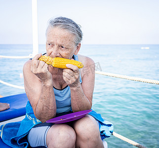 坐在海滩码头吃玉米的高级妇女