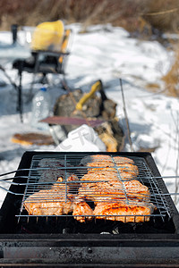 户外烧烤架摄影照片_冬季户外烧烤，在露营地野餐时用热煤烧烤牛排肉，近距离观看，露营生活方式