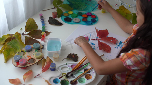 小女孩用水粉画在秋天的黄叶上，儿童艺术，儿童创造力，秋天艺术。