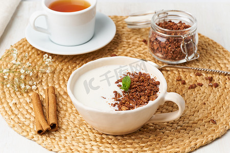 格兰诺拉麦片摄影照片_杯中装有巧克力格兰诺拉麦片的酸奶，米色背景的茶早餐，侧视图。