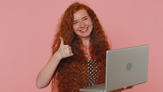 良好喜欢摄影照片_在笔记本电脑上在线工作的红发女孩表现出积极的良好反馈，例如彩票中奖