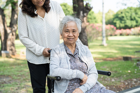 护理人员帮助和护理亚洲老年或老年老妇患者坐在公园里的轮椅上，快乐地坐着，健康强大的医疗理念。