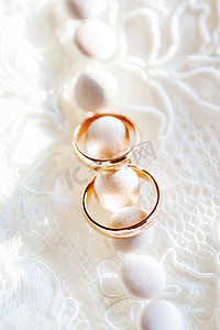 金色婚礼装饰摄影照片_蕾丝丝绸织物上的金色结婚戒指，配有按钮。