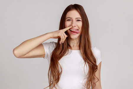 礼貌摄影照片_滑稽的女人用愚蠢的傻脸抠鼻子，拔鼻屎，不礼貌，行为不端。