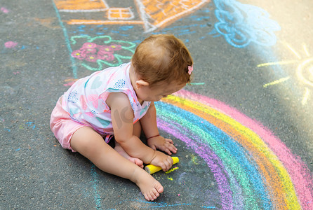 孩子用粉笔在柏油路上画了一栋房子和一条彩虹。