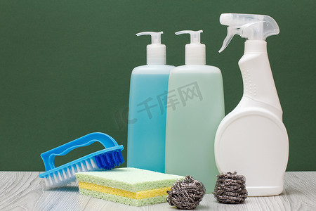 绿色背景上的瓶装洗碗液、玻璃和瓷砖清洁剂和海绵。
