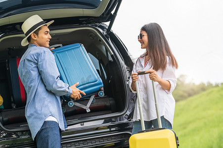 长周末旅行期间，亚洲男人帮助女人从车上提起手提箱。