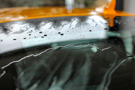 浅景深（焦点只有小水滴）黄色汽车后窗在洗车/雨中被水覆盖。