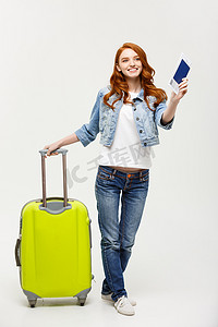 旅行和生活方式：一位兴奋的年轻白人女性的肖像，穿着夏装，手持护照和机票，站在明亮的黄色背景中，手提箱被隔离