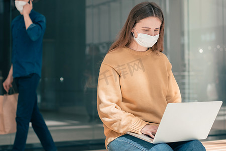 戴着防护面具的年轻女性在街上使用笔记本电脑