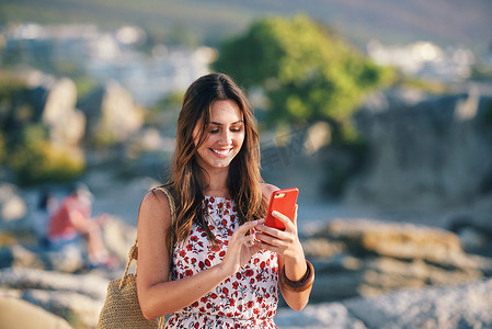 美丽的女人在日落时在海滩上使用智能手机发短信