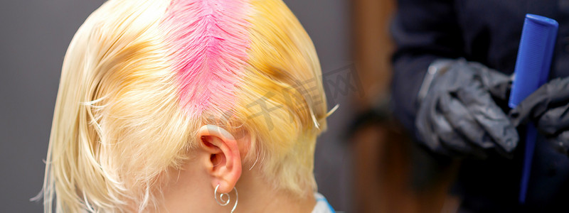 年轻的白人妇女在美容院里把发根染成粉红色。