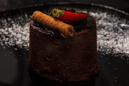 巧克力慕斯配草莓和巧克力棒放在黑色盘子上。